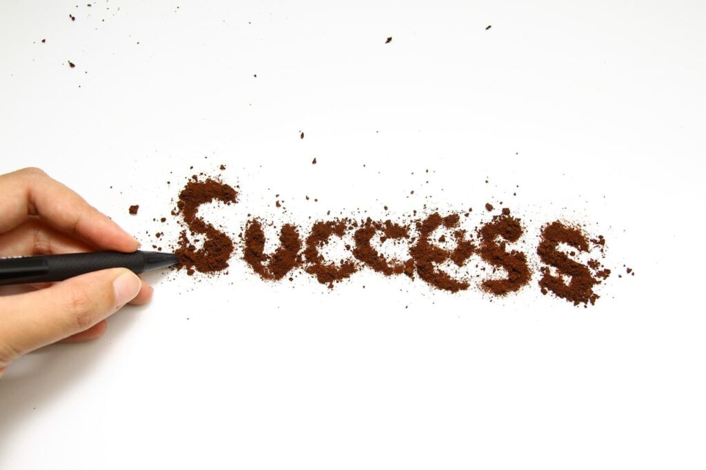 コーヒーパウダーで「Success」の文字を書いている指。